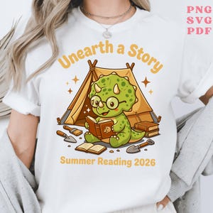 May include: White t-shirt featuring a cartoon dinosaur reading a book in front of a tent. The text "Unearth a Story" and "Summer Reading 2026" are printed in yellow. The dinosaur wears glasses and is surrounded by books and gardening tools.