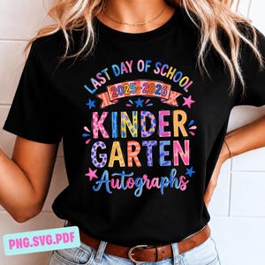Puede incluir: Camiseta negra con texto colorido que dice "LAST DAY OF SCHOOL 2025-2026 KINDERGARTEN AUTOGRAPHS". El texto es de varios colores y fuentes, con estrellas y lunares. Se ve un cinturón marrón.