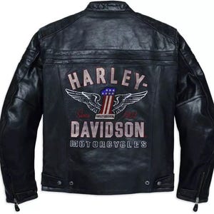 Puede incluir: Chaqueta de moto de cuero negro con el logotipo de Harley-Davidson bordado en la espalda. El logotipo presenta alas, los colores de la bandera estadounidense y las palabras "HARLEY-DAVIDSON MOTORCYCLES" y "Since 1903". La chaqueta tiene cremallera frontal y bolsillos con cremallera.