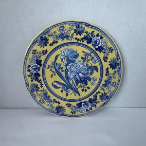 May include: A round, decorative plate with a yellow background and blue floral patterns. The plate features a central floral bouquet and a border of smaller flowers. The design is reminiscent of vintage china.