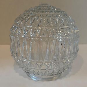 May include: Clear glass globe light fixture with a geometric, diamond-shaped pattern. The globe has a rounded shape with a tiered top and a flared base. The glass is transparent, allowing light to pass through.