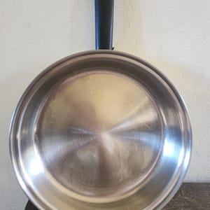 May include: A white ceramic mug with a black handle and the text "But first, coffee" in a handwritten style. The mug is on a white surface. The mug is approximately 4 inches tall.