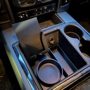 Könnte beinhalten: Schwarzer Auto-Konsolen-Organizer mit mehreren Fächern, darunter ein Getränkehalter und eine kleine Ablage. Der Organizer ist für die Mittelkonsole eines Fahrzeugs konzipiert und bietet zusätzlichen Stauraum.