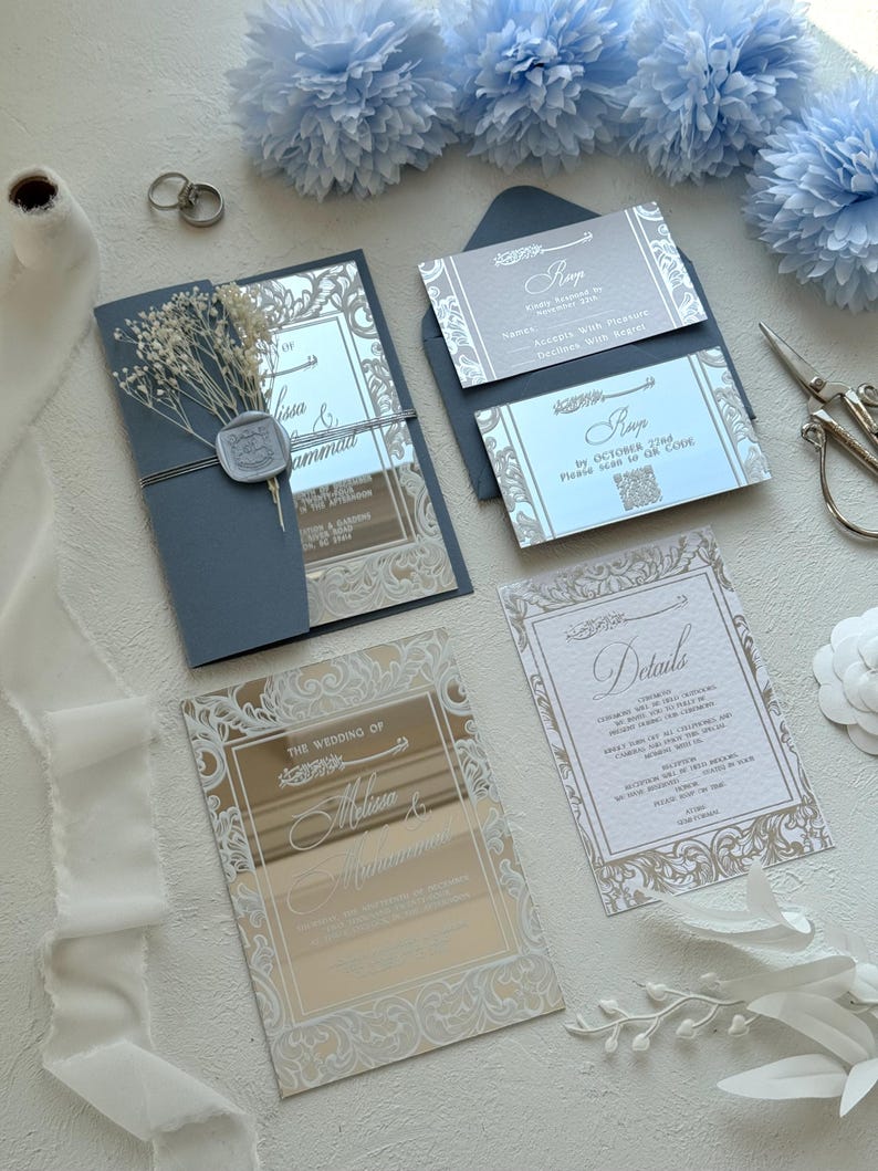 Pu&ograve; includere: Elegante suite di inviti di nozze con biglietti in acrilico a specchio e intricati disegni floreali. La suite include biglietti RSVP, biglietti di dettaglio e un invito piegato, il tutto in tonalit&agrave; argento e blu. Elementi decorativi includono fiori secchi e un sigillo di cera.