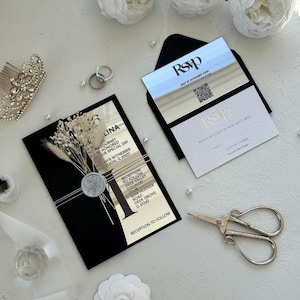 May include: Elegant wedding invitation suite featuring a black and gold mirrored invitation card with dried floral accents, a silver wax seal, and an RSVP card in a black envelope. The suite is complemented by white floral decorations and a pair of silver scissors.