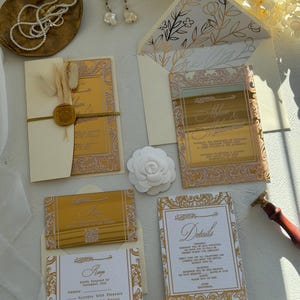 May include: Elegant wedding invitation suite featuring gold foil accents on ivory cards. Includes invitation, RSVP, and details cards. Embellished with floral designs and a wax seal. A pearl necklace and earrings are also visible.