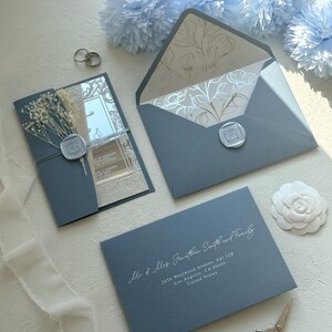 Pu&ograve; includere: Elegante set di partecipazioni di nozze in blu polveroso. Include un invito con fiori secchi, una busta con fodera floreale e una busta per l'indirizzo. La busta dell'indirizzo recita "Mr & Mrs Jonathan Smith and Family".