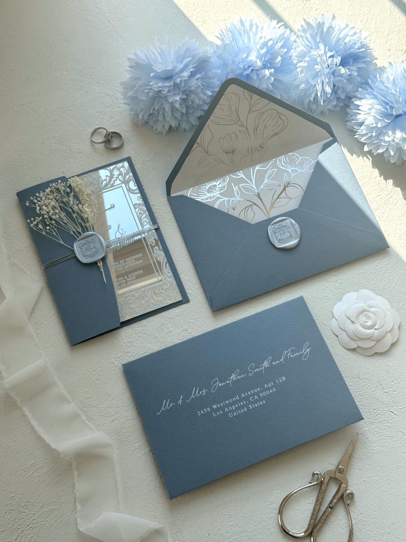 Pu&ograve; includere: Elegante set di partecipazioni di nozze in blu polveroso. Include un invito con fiori secchi, una busta con fodera floreale e una busta per l'indirizzo. La busta dell'indirizzo recita "Mr & Mrs Jonathan Smith and Family".