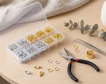 May include: A clear plastic storage container with ten compartments filled with gold and silver jump rings and lobster clasps. Beside the container are metal pliers with black handles, silver tweezers, and several loose gold and silver rings.