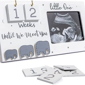 May include: White wooden baby announcement frame with a sonogram image. The frame has the text "little One" and "12 Weeks Until We Meet You". Includes gray elephant cutouts and number tiles.
