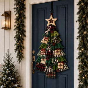May include: A fabric Christmas tree wall hanging featuring layered green and red plaid ruffles, small decorative gift boxes, and candy cane accents. The tree is topped with a beige star and hangs from a black hook on a dark blue door.