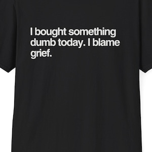 May include: Black t-shirt with the text "I bought something dumb today. I blame grief." in white. The shirt has short sleeves and a crew neck. The website DeadParents.com is printed at the top.