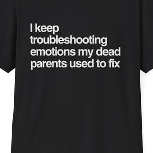 May include: Black t-shirt with white text that reads "I keep troubleshooting emotions my dead parents used to fix." The shirt has a crew neck and short sleeves. The website DeadParents.com is printed at the top.