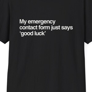 Op de afbeelding: Zwart T-shirt met witte tekst: "My emergency contact form just says 'good luck'". Het T-shirt met ronde hals is gemaakt van zacht materiaal. De website DeadParents.com staat bovenaan afgedrukt. Een casual kledingstuk voor dagelijks gebruik.