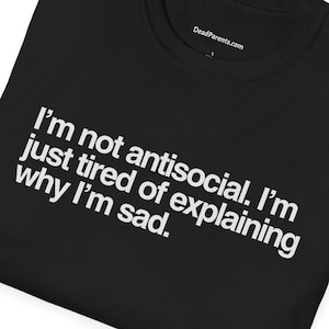 Peut inclure: T-shirt noir avec le texte "I'm not antisocial. I'm just tired of explaining why I'm sad." Le t-shirt porte également le texte "DeadParents.com" imprimé sur le col.