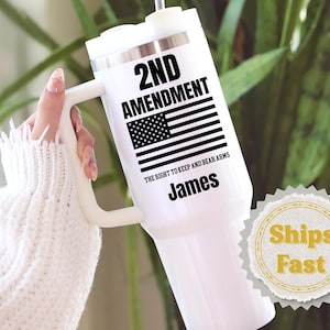 May include: White tumbler with a handle and a silver lid. The tumbler features the text "2ND AMENDMENT" above an American flag graphic, with "THE RIGHT TO KEEP AND BEAR ARMS" and the name "James" below. A straw is inserted in the lid.