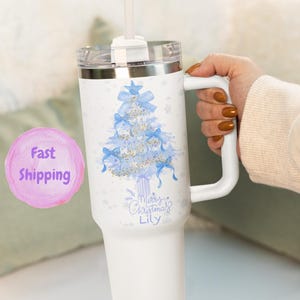May include: White insulated tumbler with a handle and a clear lid. The tumbler features a light blue Christmas tree design with bows and the text "Merry Christmas Lily". A white straw is inserted in the lid.