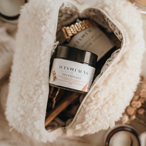 Könnte beinhalten: Ein cremefarbener, flauschiger Reißverschlussbeutel im Sherpa-Stil mit einem schwarzen Tiegel Alta Fauna Deodorant aus grasgefüttertem Talg, Sorte Citrus Grove, beschriftet mit 2 oz, sowie einer goldfarbenen Uhr und einem Holzwerkzeug im Inneren.