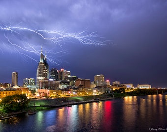 Könnte beinhalten: Eine nächtliche Skyline mit einem hohen Wolkenkratzer in der Mitte, beleuchtet von den Lichtern der Stadt. Ein dramatischer Blitzeinschlag erhellt den Himmel über der Stadt.