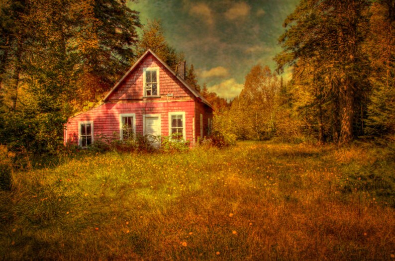 May include: A red wooden house with white trim sits in a field of tall grass. The house has three windows and a door. The house is surrounded by trees.
