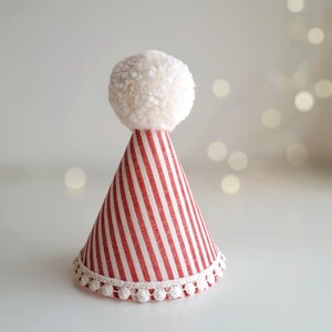 May include: A festive party hat with red and white stripes, topped with a fluffy white pom-pom. The base of the hat is trimmed with a delicate white pom-pom lace. This decorative hat is perfect for celebrations.