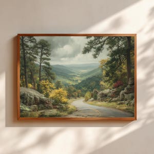 May include: A framed landscape painting depicts a winding road through a valley. The artwork features a palette of greens, yellows, and browns, with a cloudy sky overhead. The road is flanked by trees and rocky outcroppings.