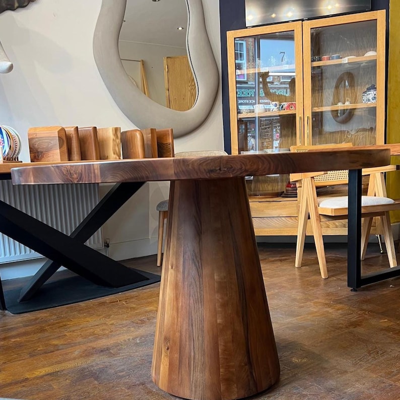 Puede incluir: Una mesa de comedor de madera maciza con tapa redonda y base c&oacute;nica. La mesa es de madera marr&oacute;n oscuro con vetas visibles. La mesa tiene aproximadamente 100 cm de di&aacute;metro y 76 cm de altura.