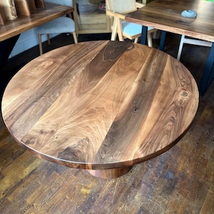 Puede incluir: Una mesa redonda de madera con un acabado de vetas naturales. La mesa tiene una base de pedestal y una superficie lisa y pulida. Los tonos de madera var&iacute;an de marr&oacute;n claro a oscuro, creando una est&eacute;tica c&aacute;lida. La mesa es adecuada para comer o como pieza decorativa, con unos 100 cm de di&aacute;metro.