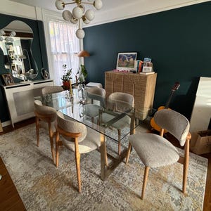 May include: A modern dining room set with a rectangular glass table and six upholstered chairs. The chairs have wooden legs and curved backs. The room features a rug, a cabinet, and a mirror.