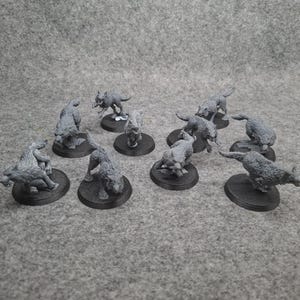 May include: Nine grey wolf miniatures, each on a black circular base, in various poses. Some are standing, others crouching, giving a dynamic feel. Suitable for tabletop gaming or miniature collecting. The bases are approximately 2.5 cm in diameter.