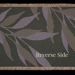 Reverse side of the Olive Branch woven cotton throw blanket laid flat, showing muted botanical leaves on a dark woven field with multi color fringe on all sides.