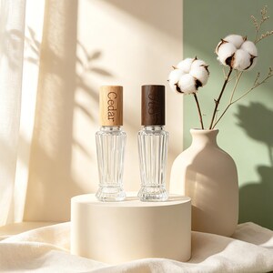 May include: Two clear glass spray bottles with vertical ribbed textures and cylindrical wooden caps. The left cap is light wood with the word Cedar engraved, and the right cap is dark wood with an engraved script monogram.