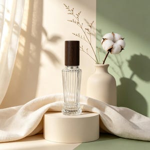 May include: A clear glass bottle with vertical ribbed detailing and a dark brown wooden cylindrical cap. The bottle features a tapered neck and a flared base, standing upright on a circular platform, showcasing a refined and functional design.