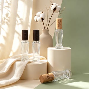 May include: Four clear glass perfume bottles with vertical ribbed textures and wooden caps. Two bottles have dark brown caps, while two have light wood caps. One light wood cap is engraved with the word Cedar and another with the letter K.