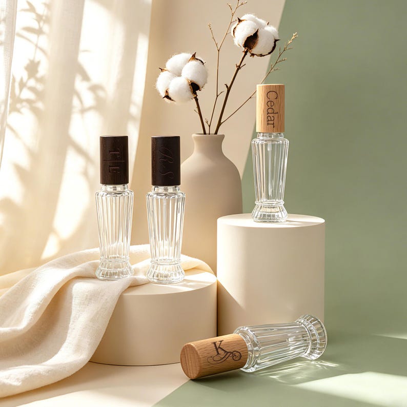 May include: Four clear glass perfume bottles with vertical ribbed textures and wooden caps. Two bottles have dark brown caps, while two have light wood caps. One light wood cap is engraved with the word Cedar and another with the letter K.