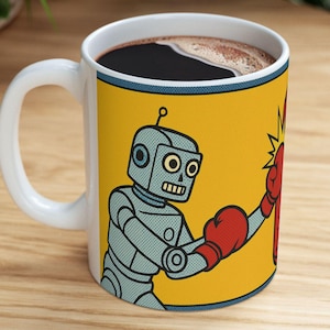 Peut inclure: Mug en céramique blanche avec une illustration de robot de dessin animé boxant un autre robot. Le mug a un fond jaune avec une bordure bleue et une anse blanche. Les robots sont gris et rouges, avec des gants de boxe.