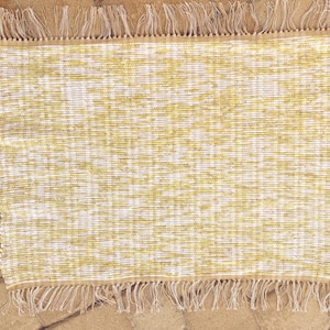 May include: A woven rug with a white and yellow pattern and fringe on all sides.