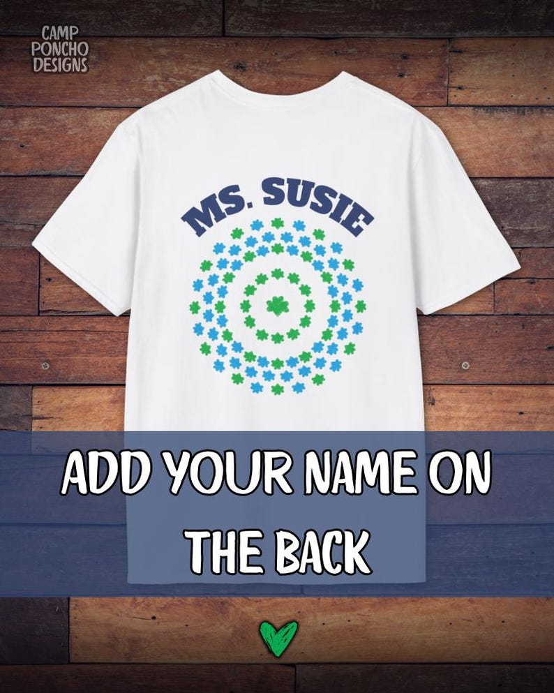 May include: White t-shirt with the text "MS. SUSIE" in blue, above a circular design of green and blue shapes. The bottom of the shirt has the text "ADD YOUR NAME ON THE BACK". A green heart is at the bottom.