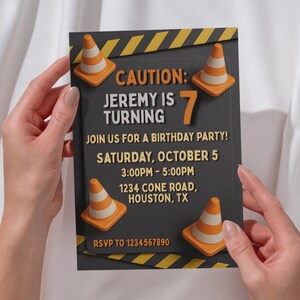 Puede incluir: Una invitación de cumpleaños con temática de construcción. La invitación es de color gris oscuro con detalles en naranja y amarillo, con conos de tráfico y el texto "CAUTION: JEREMY IS TURNING 7". Incluye detalles de la fiesta.