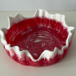 May include: A decorative bowl with a wavy rim. The bowl features a vibrant red interior with white marbling, and the rim is white. The bowl is likely made of ceramic or a similar material.