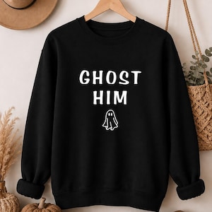 May include: A black long-sleeve crewneck sweatshirt featuring the white text GHOST HIM centered on the chest, accompanied by a small white line-art illustration of a ghost positioned directly below the text.