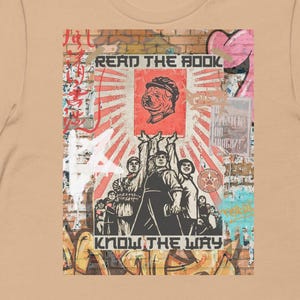 May include: Tan short-sleeve t-shirt featuring a graphic design with the text "READ THE BOOK" and "KNOW THE WAY". The design includes a red and white background with a dog's head and figures raising their arms.