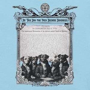 Puede incluir: Camiseta azul claro con una parodia de la Declaración de Independencia. La imagen presenta perros vestidos con ropa colonial y el texto "ON THIS DAY. THE PACK BECAME SOVEREIGN" y "In CONGRESS July 4, 1776". También se ve el logotipo de Pupaganda Prints.