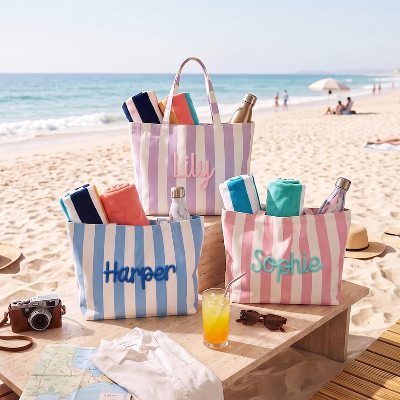 Peut inclure: Trois sacs fourre-tout en toile ray&eacute;e avec les noms brod&eacute;s Lily, Harper et Sophie. Chaque sac contient des serviettes roul&eacute;es et une bouteille d'eau. Les sacs sont violet clair, bleu clair et rose clair avec des rayures verticales blanches.