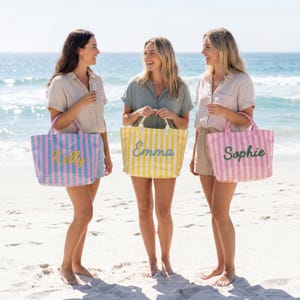 May include: Three rectangular tote bags with vertical stripes. The first bag is blue and pink with the name Kelly in yellow. The second bag is yellow and white with the name Emma in green. The third bag is pink and white with the name Sophie in green.