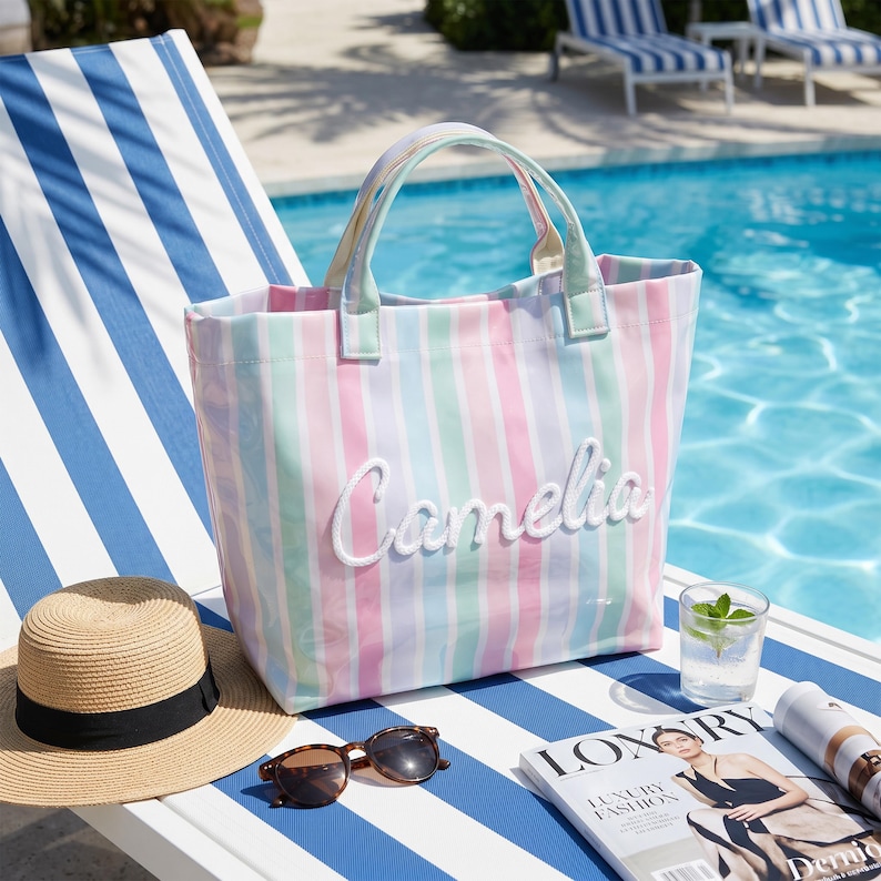 May include: A tote bag featuring vertical pastel stripes in pink, blue, and green with the name Camelia embroidered in white script on the front. The bag has two matching striped handles and a structured rectangular shape for carrying items.