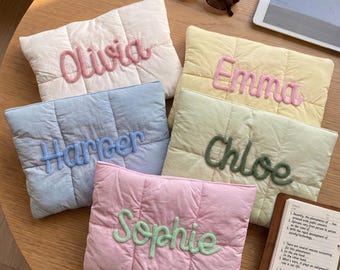 May include: Five rectangular quilted pouches in pastel colors, each featuring a name in raised, textured yarn lettering. The pouches are white with 'Olivia', yellow with 'Emma', light blue with 'Harper', light green with 'Chloe', and pink with 'Sophie'.