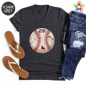 May include: Dark grey V-neck t-shirt featuring a distressed baseball graphic with the number 26 and a heart. The shirt is paired with blue jeans and brown sandals. The text "H.DARK GREY" is in the upper left corner.