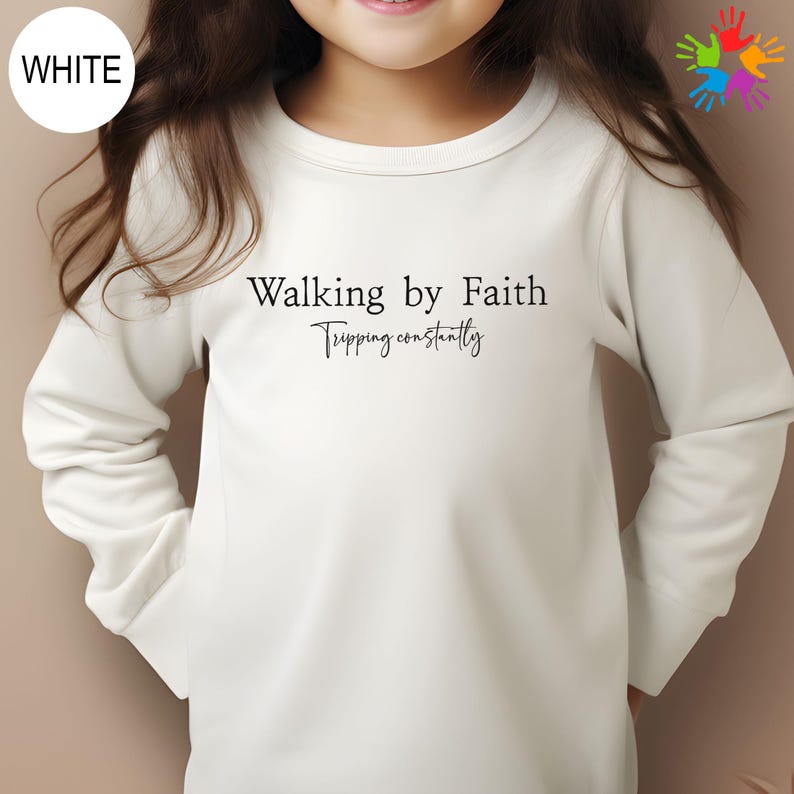 A young girl wearing a white long-sleeved shirt with the text "Walking by Faith" printed on it.