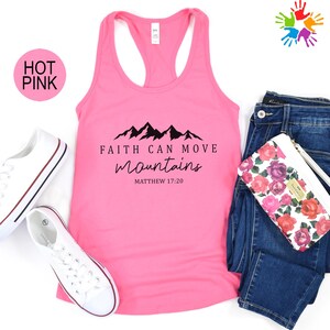 A pink tank top with the text "Faith can move mountains" printed on it, along with a pair of jeans and a floral wallet.